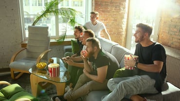 5 men in their 20s engage and watch something on a tv screen 